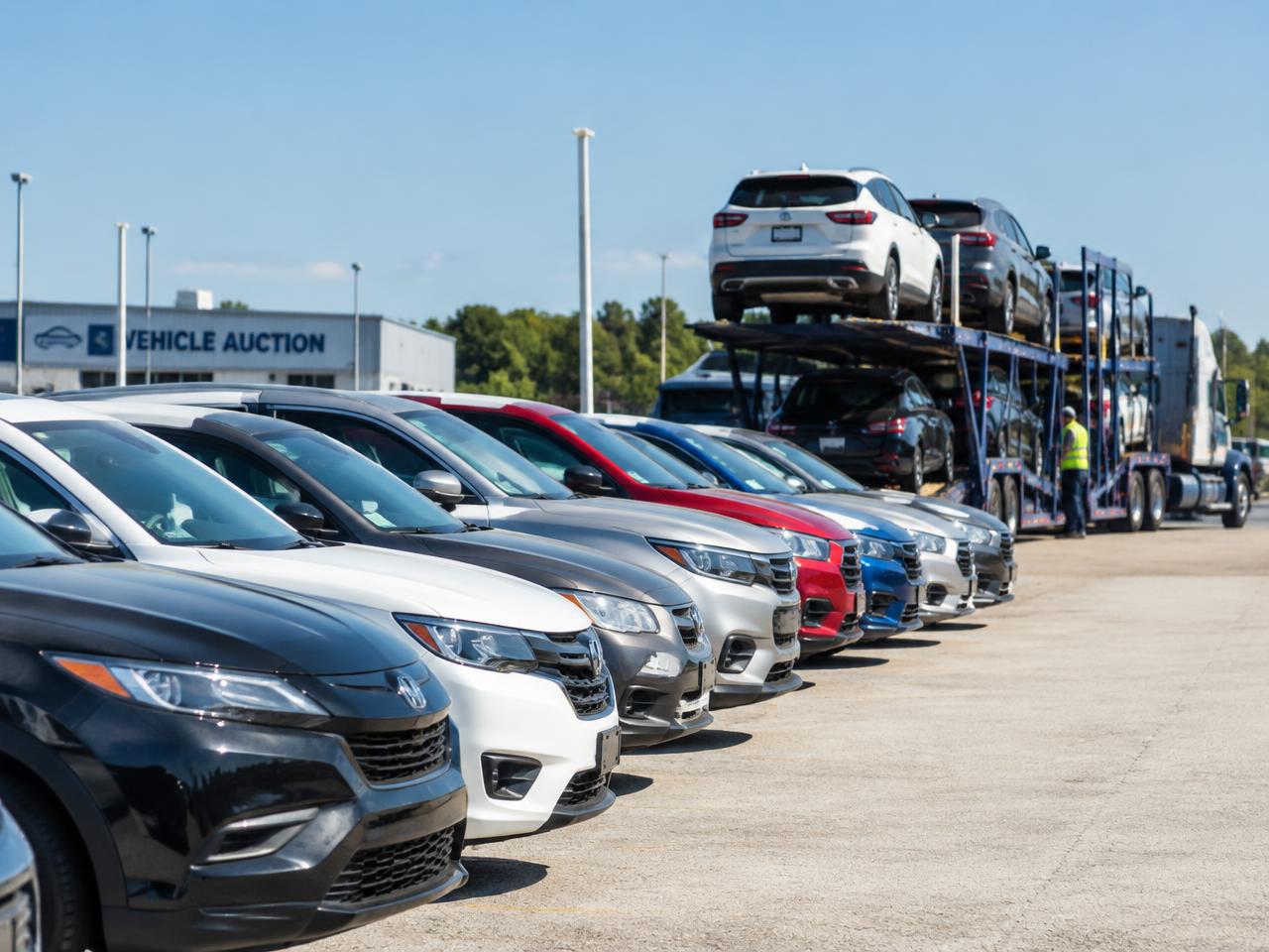 Vehicles lined up at an auction lot with a car carrier loading